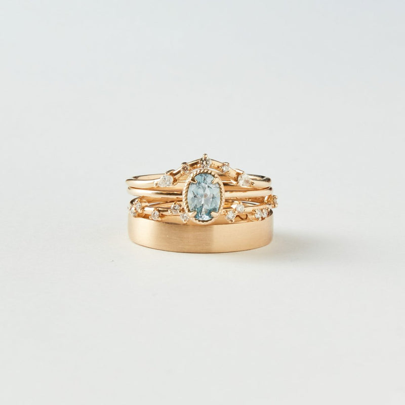 A close-up image showcases the "golden glow one-of-a-kind ring" from "beloved by bluboho," featuring a central 14k yellow gold ring with a cyan green oval sapphire surrounded by small diamonds, accompanied by two matching gold bands with intricate detailing, all set against a plain white background.