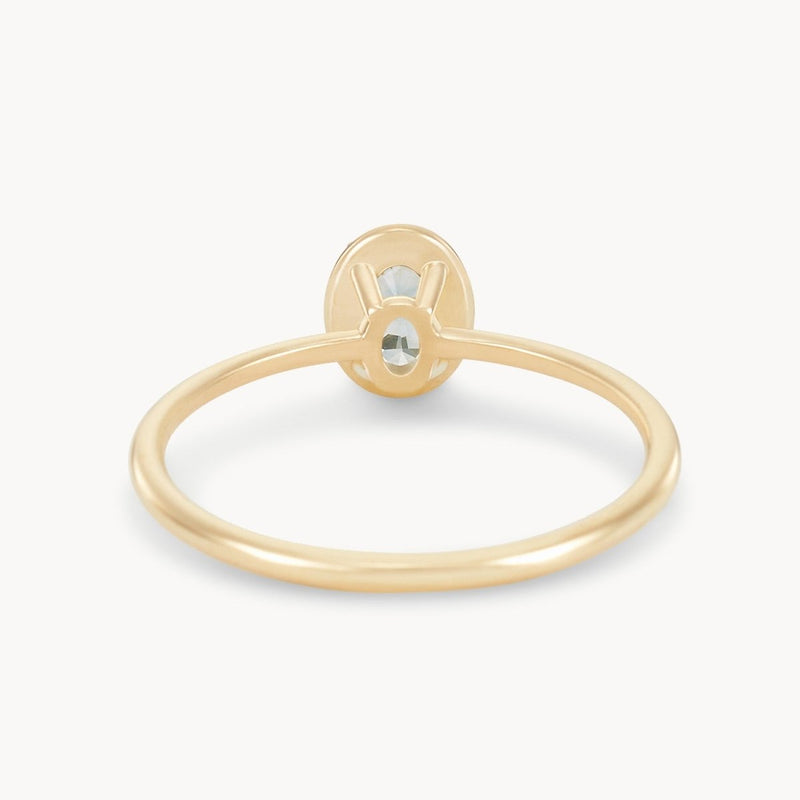 The delicate golden glow one-of-a-kind ring by beloved by bluboho is pictured, showcasing a minimalist design with a small, horizontally set cyan green oval sapphire in a bezel setting. The ring's thin 14k yellow gold band contrasts elegantly with the gemstone's understated sparkle.