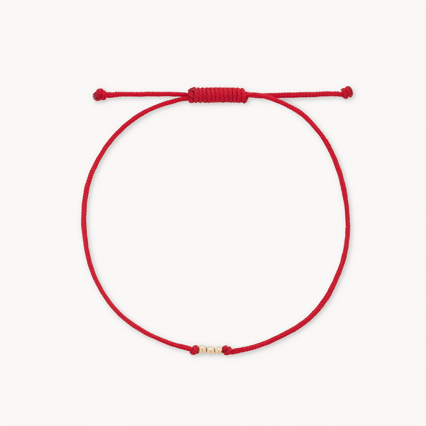 The abacus contemplation cord bracelet by bluboho is a minimalistic accessory featuring a red cord with an adjustable knot. The bracelet showcases delicate 10k yellow gold bead detail near the center, with the ends neatly finished with small knots.