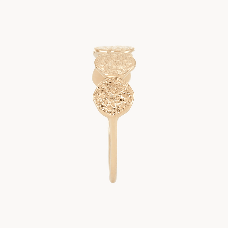 A **bluboho abacus disk ring - 14k yellow gold** featuring a design of three textured, round discs arranged in a vertical line on a thin, smooth band. The ring has an elegant and minimalist appearance, highlighted by its delicate craftsmanship and shiny finish.