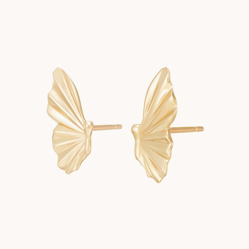 The metamorphosis butterfly wing earrings by bluboho are crafted from 14k yellow gold and designed to resemble intricate butterfly wings with detailed lines and curved edges. These earrings feature stud posts for secure attachment. The backdrop is a simple white.