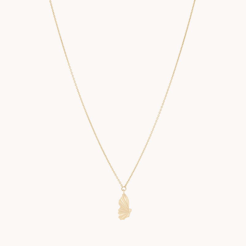 The metamorphosis butterfly wing necklace by bluboho features a delicate 14k yellow gold fine chain and a pendant shaped like a butterfly wing. The minimalist design accentuates the intricate details of the wing, highlighted by the gold material, while the plain background emphasizes the necklace's elegance.