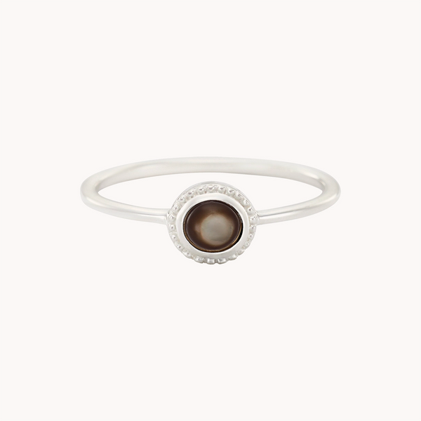 The full moon dark mother of pearl ring by bluboho is a simple silver piece with a thin band and a dark round mother of pearl gemstone set in the center. The gemstone is encircled by a delicate, textured silver border and is displayed against a plain white background.