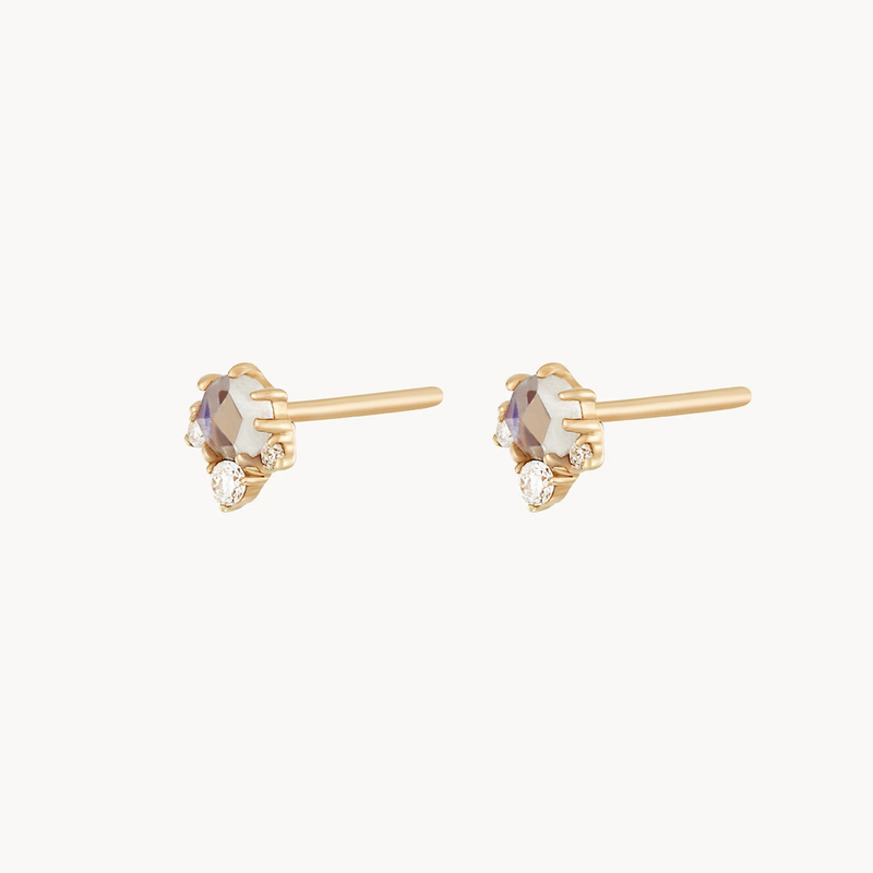 A pair of bluboho's Full Moon Glow Diamond Moonstone Earrings. Each delicate gold stud features a central, faceted moonstone gemstone with smaller, round diamonds accenting it, set against a white background.