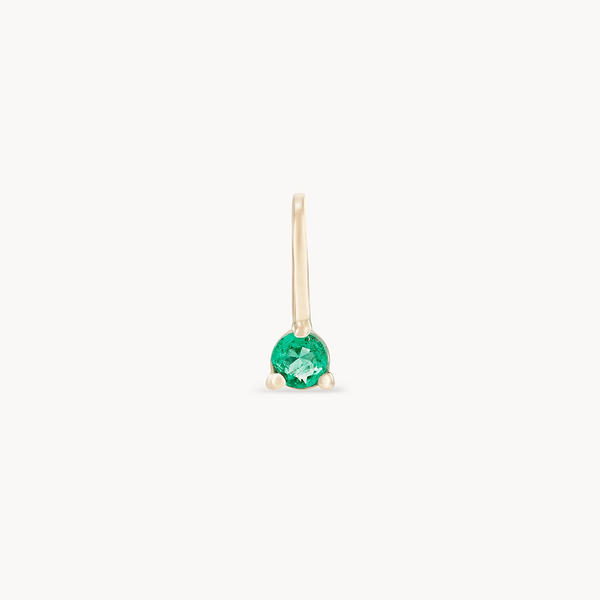 The serendipity may birthstone charm by bluboho is an elegant 10k yellow gold earring, featuring a single round emerald gemstone secured by three delicate gold prongs. Its minimalist and refined design includes a sleek and slender gold hook for attaching to the ear.