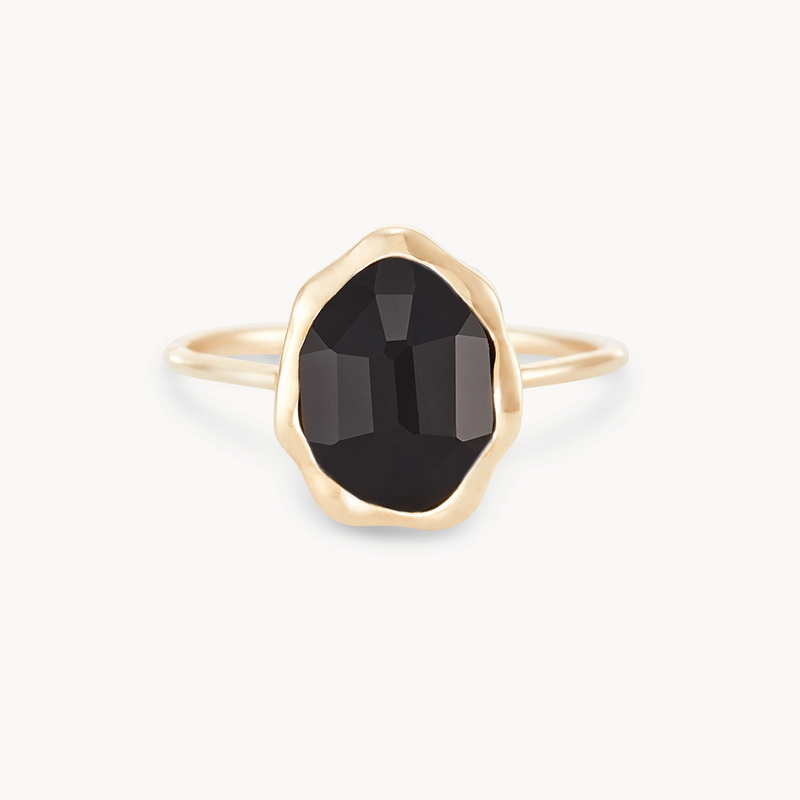 The bluboho black onyx mood ring features an irregularly shaped black onyx stone with faceted cuts, set in a smooth, slightly wavy 14k yellow gold bezel. The thin band perfectly complements the prominent gemstone. Displayed against a plain white background, the elegant design of the ring stands out beautifully.