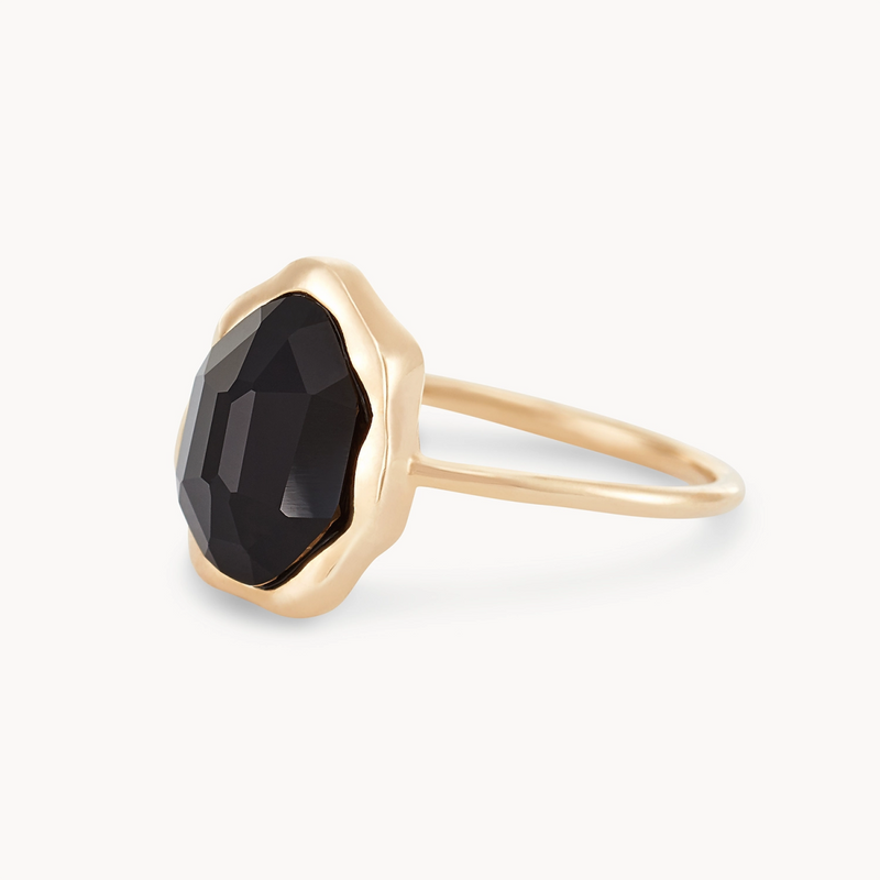 Introducing the "black onyx mood ring - 14k yellow gold" by bluboho: This exquisite piece features a large, faceted black onyx gemstone set in a delicate scalloped bezel. The thin band of 14k yellow gold enhances its simple, elegant design and perfectly complements the bold, dark stone. The facet cuts of the black onyx give it a captivating, multifaceted sparkle.