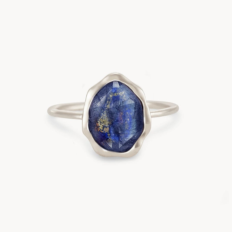 A sterling silver lapis lazuli mood ring by bluboho sits centered against a white background, featuring a raw, oval-shaped blue gemstone adorned with unique golden specks. The gemstone's irregular surface enhances its rustic charm, while the simple and delicate band highlights its beauty.