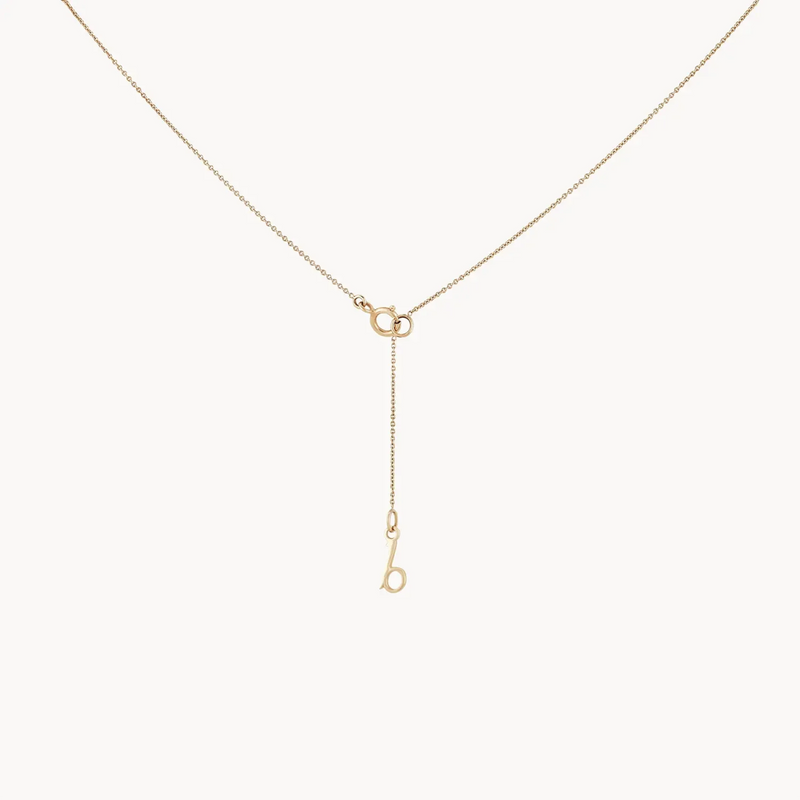 A delicate necklace by bluboho features a fine chain with two interlocked loops at the center, from which a single chain dangles down. The dangling chain holds a lowercase "b" charm at its end, creating an elegant and minimalist design. The piece is named the crescent moon tie dye necklace - 14k yellow gold.