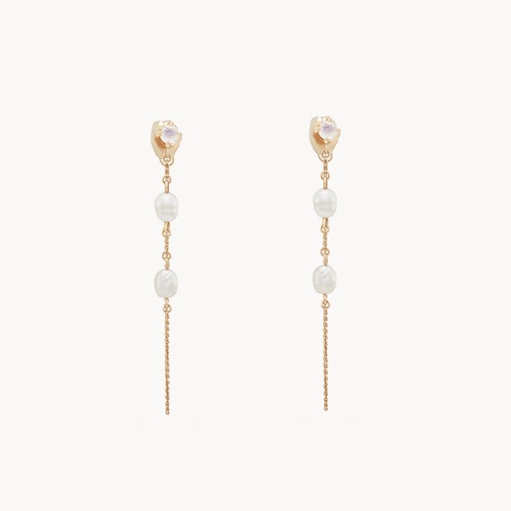 A pair of bluboho's Luna Perla Pearl Chain Earrings in 14k yellow gold, showcasing a small round crystal at the top, adorned with two white pearl-like beads along a delicate gold chain, and finished with a thin golden tassel extending from the bottom. The earrings are elegantly displayed on a plain white background.