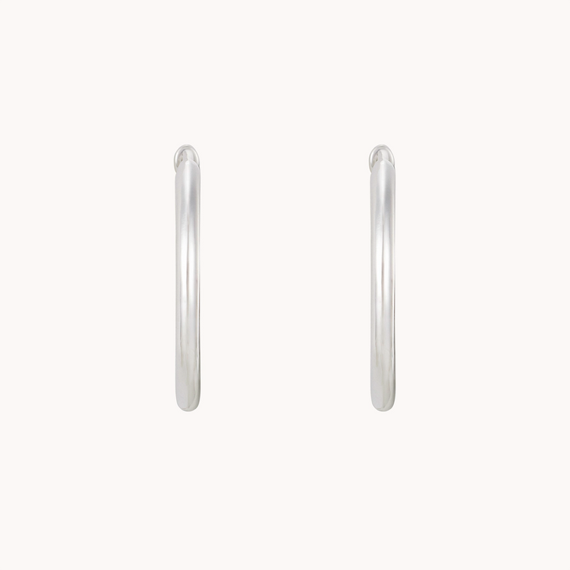 A pair of bluboho's dagger large hoop silver earrings against a plain white background. The hoops are smooth and cylindrical, featuring a polished finish.