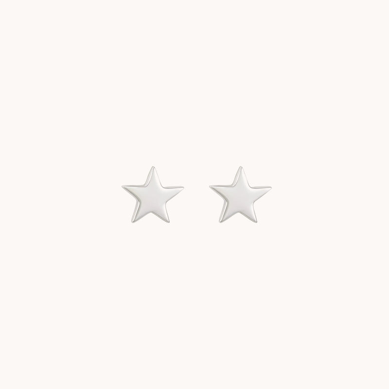 A pair of Stella earrings in sterling silver by Bluboho is displayed against a plain, light-colored background. These small, star-shaped stud earrings have a smooth, glossy finish.