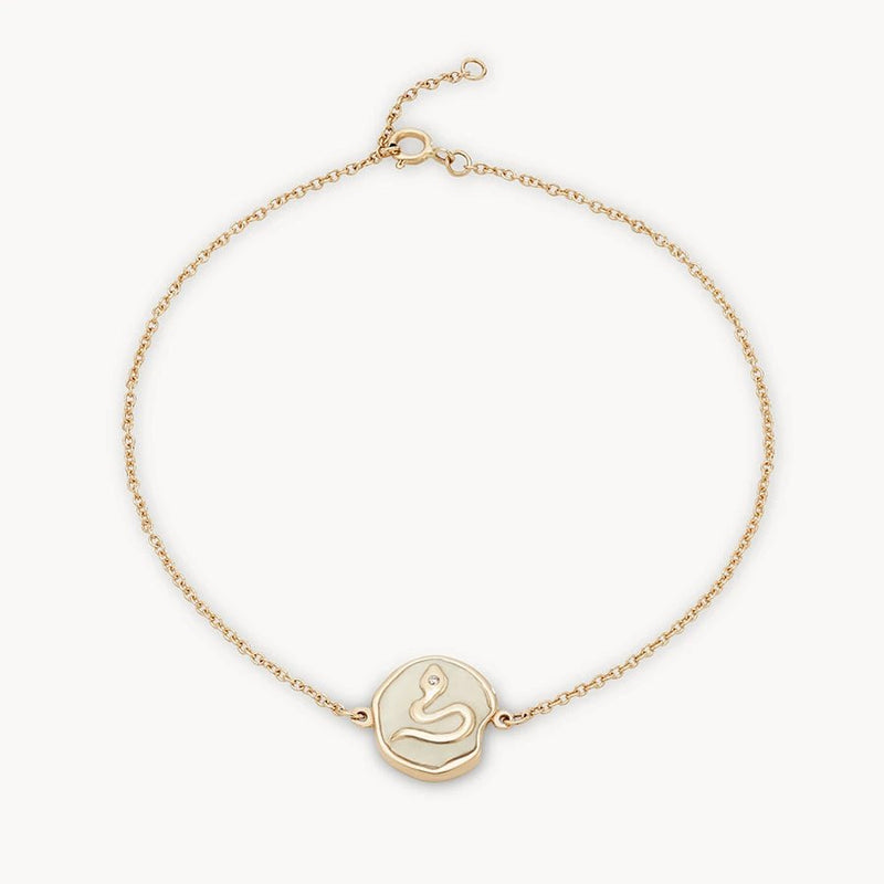 The revival snake enamel bracelet by bluboho, crafted from 14k yellow gold and accented with a diamond, features a delicate chain with a circular pendant showcasing an embossed serpent design at the center. The bracelet also includes an adjustable clasp.