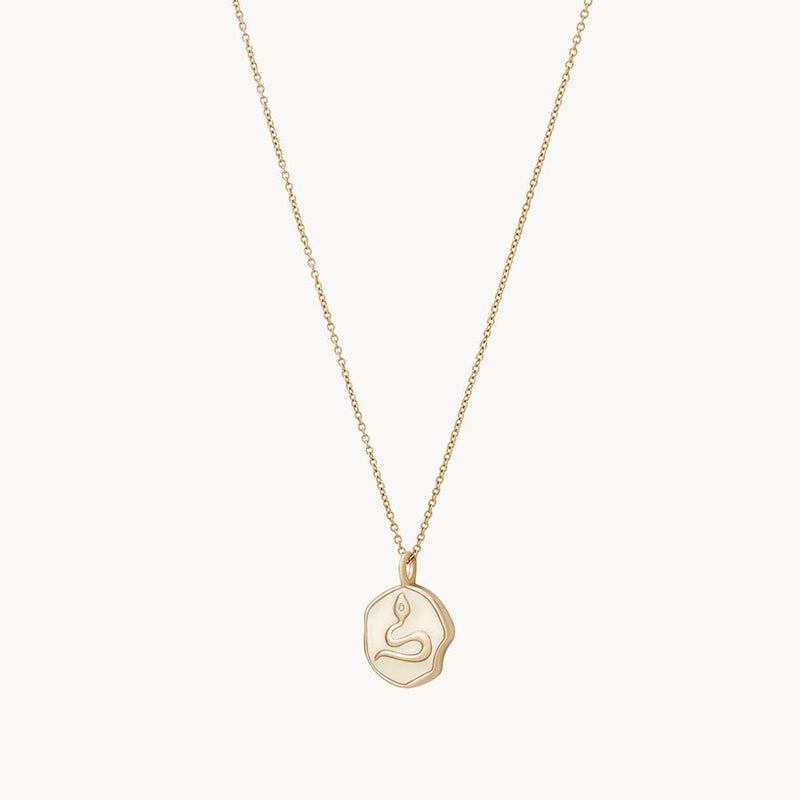 The revival snake enamel necklace by bluboho, crafted in 14k yellow gold and adorned with a diamond, features a delicate chain and an intricately designed pendant with minimalist engravings that invoke a sense of tranquility akin to a meditative pose, against a plain white background.