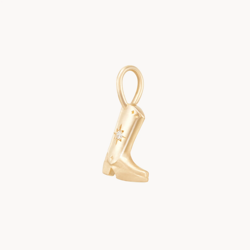 A small gold charm in the shape of a cowboy boot, adorned with a tiny star on the side detail. The boot has a loop at the top for attaching to a bracelet or necklace. The background is plain white.

Product Data:
  Product Name: abundance boot charm - 10k yellow gold, diamond
  Brand Name: bluboho