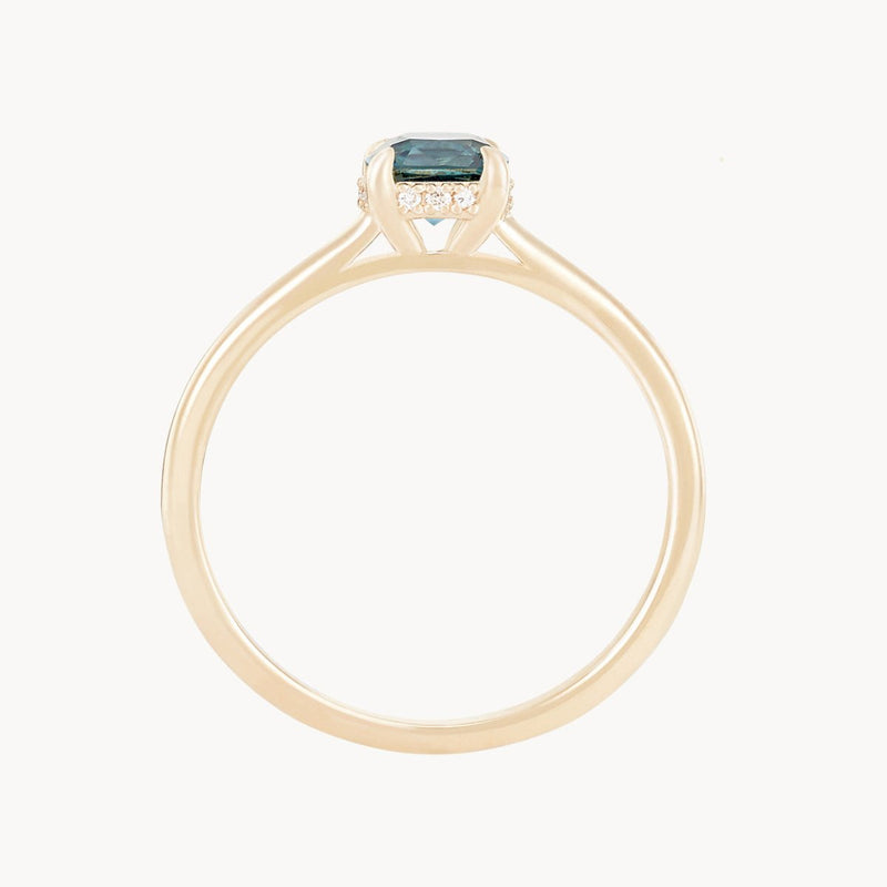 The *daydream bliss one-of-a-kind ring* by *beloved by bluboho* features a minimalist 14k yellow gold band with a cushion cut blue sapphire, elegantly surrounded by small clear diamonds in a prong setting. The design focuses on the single main gemstone, combining simplicity and elegance.