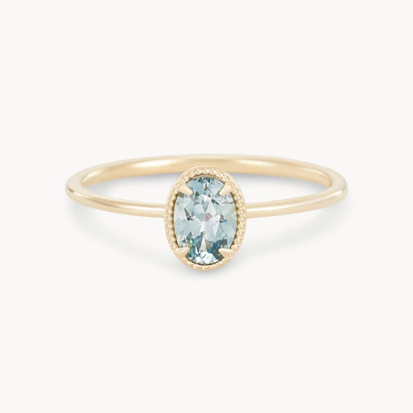 The Golden Glow One-of-a-Kind Ring by Beloved by Bluboho showcases a cyan green oval sapphire in a minimalist setting. The sapphire is accented with a fine beaded edge, highlighting its subtle hue. The ring features a thin, elegant 14k yellow gold band that perfectly complements the central gemstone.