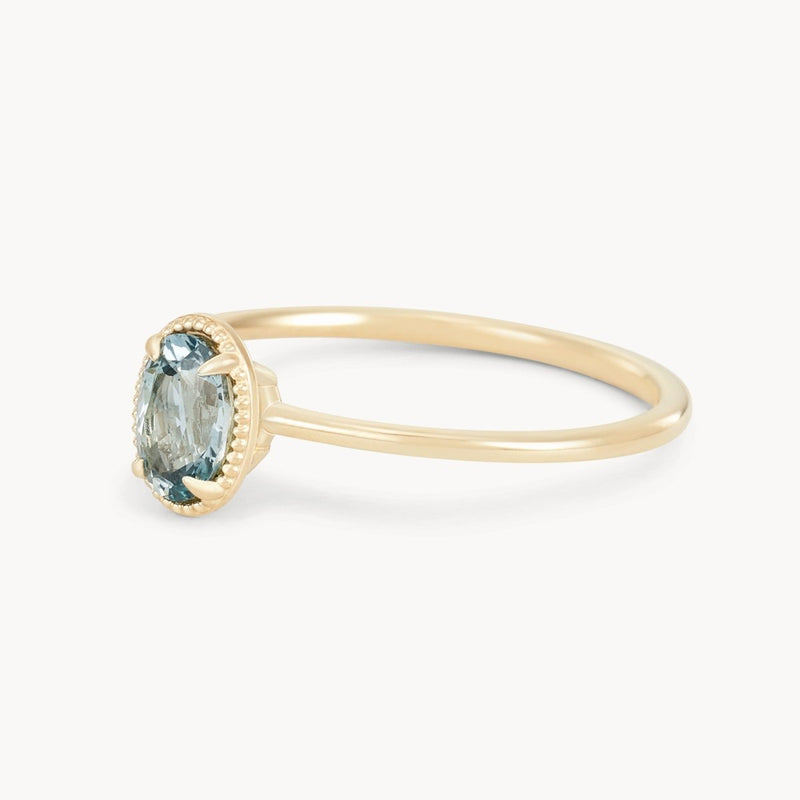 The "Golden Glow One-of-a-Kind Ring" by Beloved by Bluboho features a single oval-shaped cyan green sapphire at its center, set in a minimalist prong setting. The 14k yellow gold band is slender and smooth, accentuating the ring’s elegant design against a plain white background.