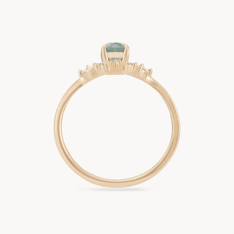 The Love’s Unity One-of-a-Kind ring by Beloved by Bluboho features a prominent cyan green oval sapphire set in a bezel. The 14k yellow gold band is slim and delicate, showcasing the unique hue of the central stone. The side view highlights the gemstone's raised setting and the sleek design of this elegant piece.