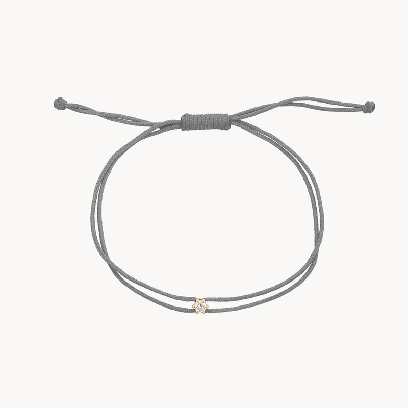 Introducing the nova diamond grey cord bracelet by bluboho: This minimalist and adjustable bracelet features a grey nylon cord with a knotted closure for easy resizing. The central charm is a small, round 10k yellow gold piece adorned with a diamond, adding a subtle and elegant touch to its simple design.