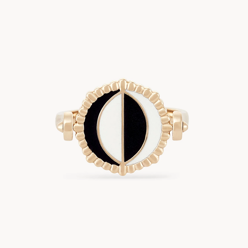 Introducing the moon phase flip enamel ring by bluboho: a 14k yellow gold masterpiece showcasing a circular design with a striking black and white half-moon motif at its core, elegantly divided by a vertical gold line. The circle's edge is beautifully adorned with small, evenly spaced gold accents, while the band boasts a smooth, shiny finish. Crafted with mother of pearl and enamel, this ring embodies elegance and sophistication.