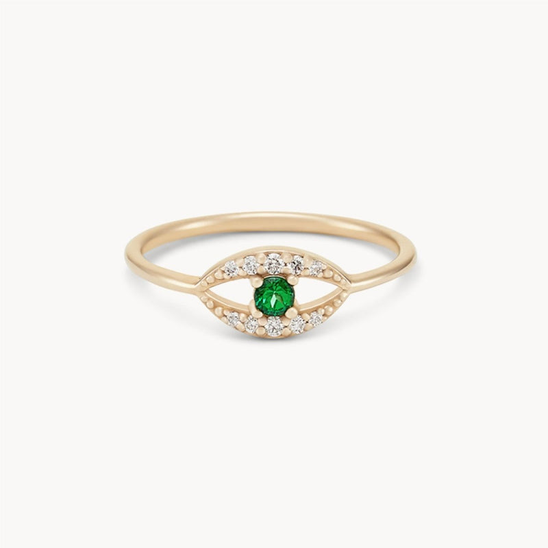 The tsavorite mystical evil eye ring by bluboho, crafted from 14k yellow gold, features a central tsavorite garnet encased within a marquise-shaped design adorned with small, sparkling white stones. The slim band accentuates the intricate arrangement of the gems, lending the ring an elegant and sophisticated appearance.