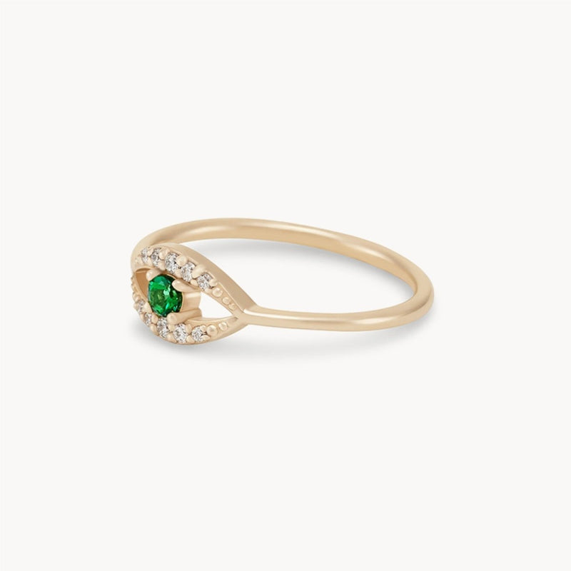 The tsavorite mystical evil eye ring by bluboho, made of 14k yellow gold, features an open band design with a striking tsavorite garnet at its center, flanked by small clear stones. The thin band elegantly curves around the vibrant green gemstone, creating a modern and delicate appearance.