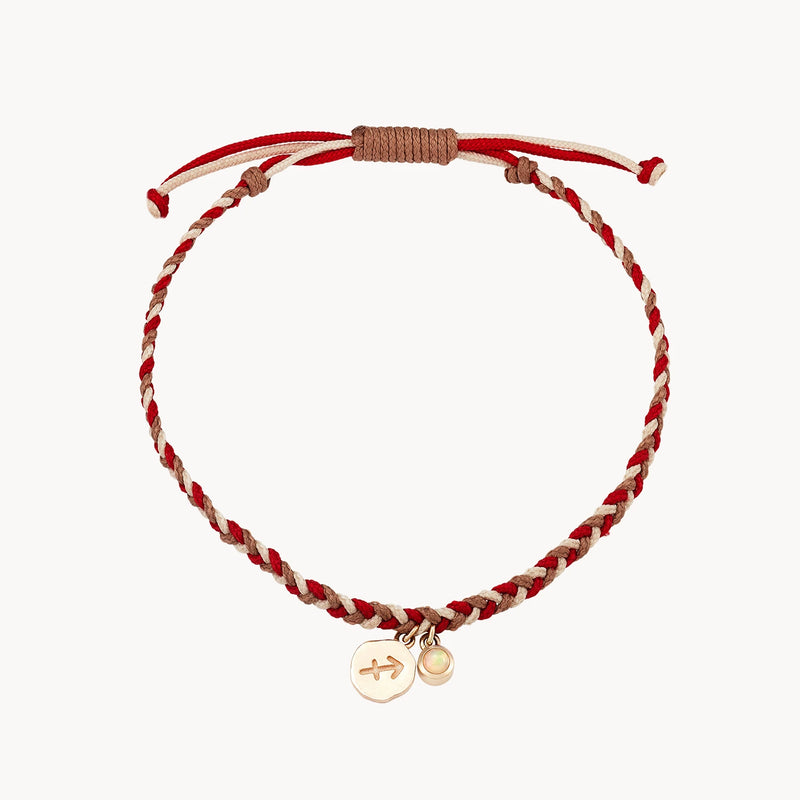 A braided bracelet featuring alternating red and beige threads. It has an adjustable knot closure and two small charms attached; one with an engraved arrow, and the other a small circular disc.

Sagittarius zodiac fire element cord bracelet - 10k yellow gold, opal, cord by bluboho